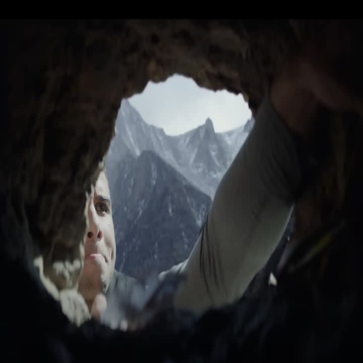 A man reaches his hand inside a small cliffside cave.