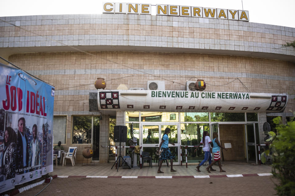 People walk past the entrance of the Cine Neerwaya, one of the movie theaters that will present films during the FESPACO (Pan-African Film and Television Festival) in Ouagadougou, Burkina Faso, Friday, Feb. 24, 2023. Most film festivals can be counted on to provide entertainment, laced with some introspection. The weeklong FESPACO that opens Saturday in violence-torn Burkina Faso's capital goes beyond that to also offer hope, and a symbol of endurance. (AP Photo/Sophie Garcia)