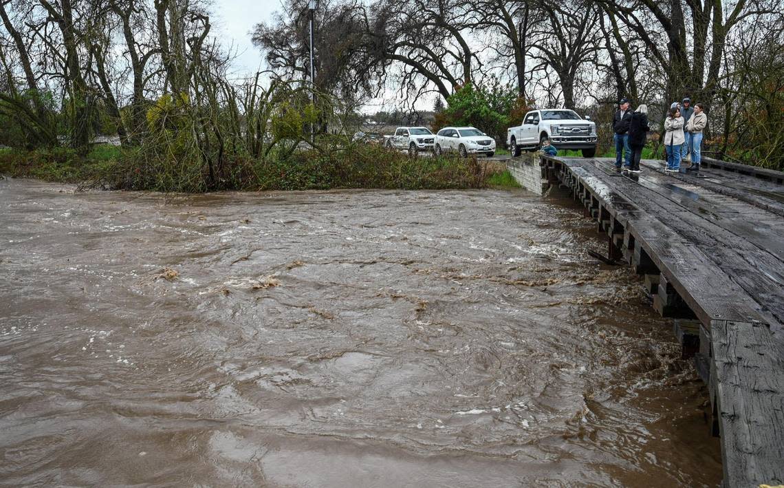 Residents living near Rio Vista Road on the Kings River in eastern Fresno County watch a swollen creek as water passes below a wooden bridge after heavy rain and mountain runoff inundated the area on Friday, March 10, 2023.