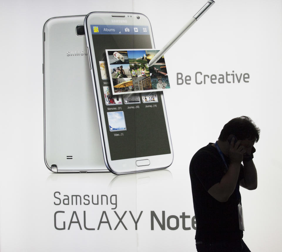 A man uses a cell phone as he stands in front of a display of the new Samsung Galaxy Note II smart phone during a media preview at the Samsung stand at the IFA consumer electric fair in Berlin, Thursday, Aug. 30, 2012. (AP Photo/Markus Schreiber)