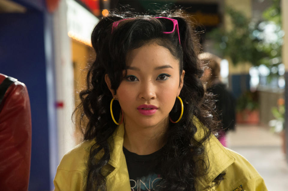 Lana Condor wears a yellow jacket and large earrings; hairstyle with pink headband