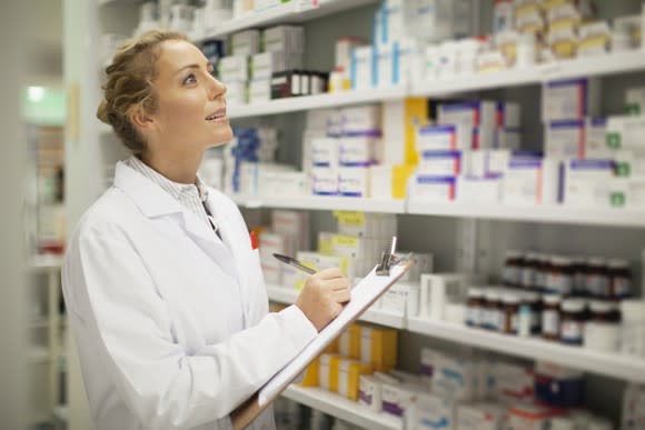 A female pharmacist with a clipboard looking at shelves of medicine.