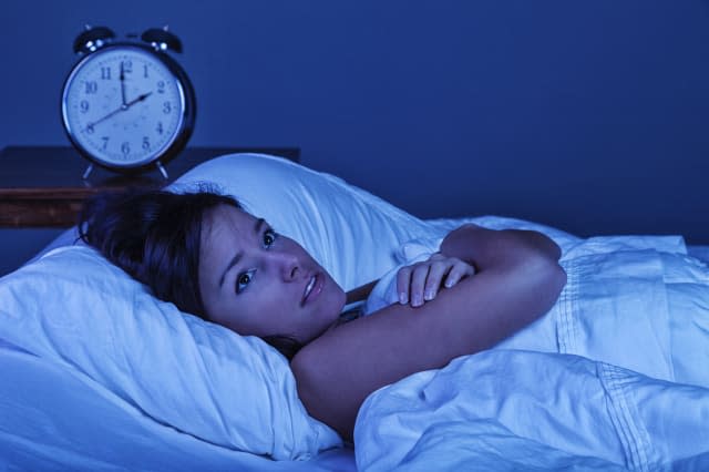 Photo of a young woman suffering from insomnia. Blue night time effect created with blue gel over studio lighting.