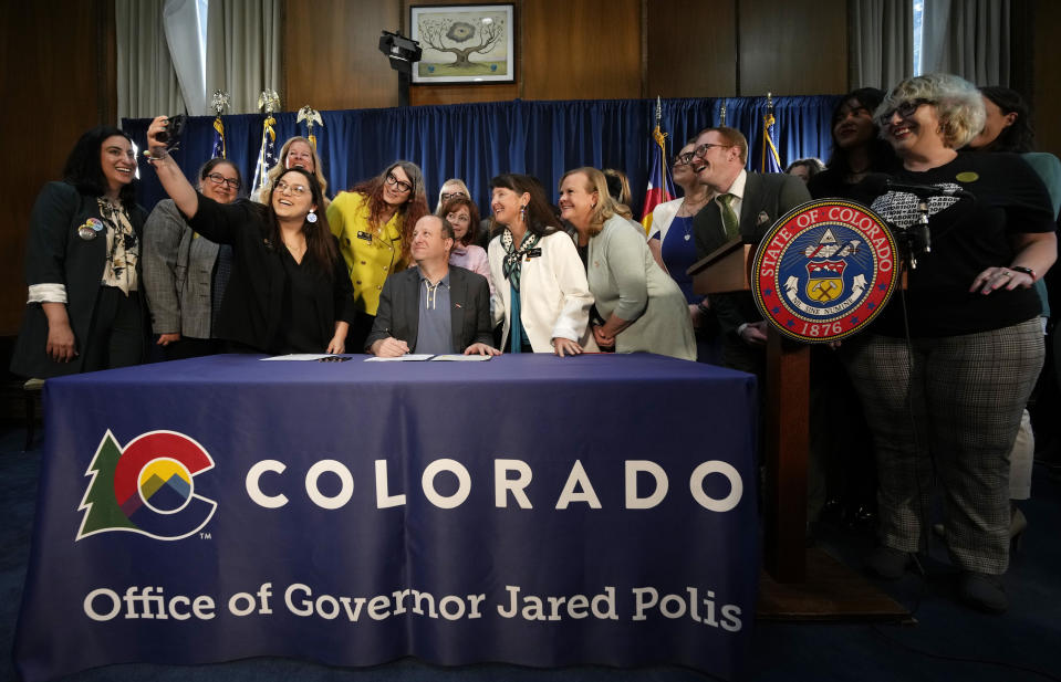 FILE - Colorado State Sen. Julie Gonzales, third from left, takes a photo of state Rep. Brianna Titone, Colorado Gov. Jared Polis, state Sen. Sonya Jaquez Lewis and state Rep. Meg Froelich and others before Polis signed the first of three bills that enshrine protections for abortion and gender-affirming care procedures and medications, April 14, 2023, in the State Capitol in Denver. The owner of a Catholic clinic challenging Colorado’s new ban on unproven treatments to reverse medication abortions has testified that the state’s pledge not to enforce it for now was not enough to protect her staff and patients. (AP Photo/David Zalubowski,File)