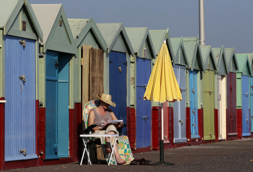 A woman reads as she sits outside a beach hut in Brighton