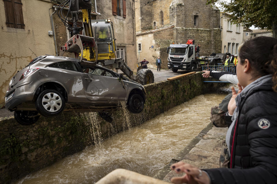 Residents watch workers pulling a car out of a torrent after flash floods in the town of Villegailhenc, southern France, Monday, Oct.15, 2018. Flash floods tore through towns in southwest France, turning streams into raging torrents that authorities said killed several people and seriously injured at least five others. (AP Photo/Fred Lancelot)