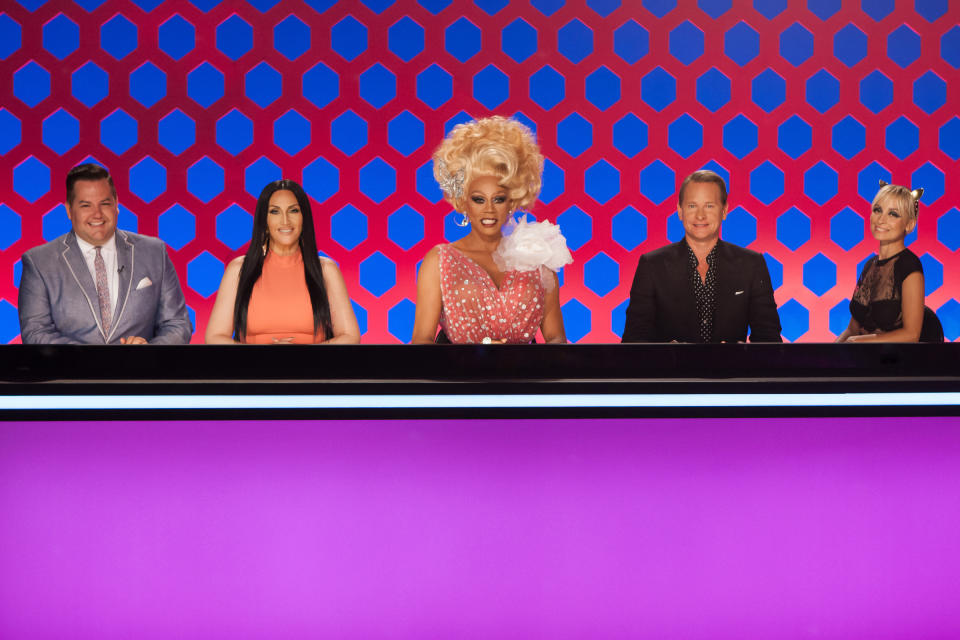 Ross Mathews, Michelle Visage, RuPaul, Carson Kressley, and a guest judge are seated at the judges' panel. RuPaul wears an eye-catching, glamorous dress