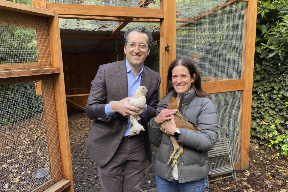 Ron and Allison Abta hold hens in front of their backyard chicken run in Ross, Calif., Dec. 15, 2020. The coronavirus pandemic is coming home to roost in America's backyards. Forced to hunker down at home, more people are setting up coops and raising their own chickens, which provide an earthy hobby, animal companionship and a steady supply of fresh eggs. (AP Photo/Terry Chea)