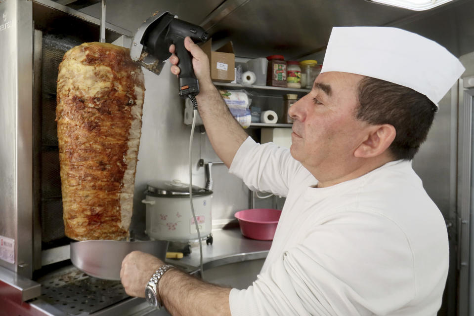 In this March 23, 2017 photo Alihan Turgut owner of a kebab stand cuts meat during an interview with The Associated Press in Wiener Neustadt, Austria. Turgut is paying the price for something that he says has not been a previous problem. His German is rough after more than 25 years in Austria, and Mayor Klaus Schneeberger says that makes him someone “whom we don’t need,” in the city of 35,000, south of Vienna. (AP Photo/Ronald Zak)