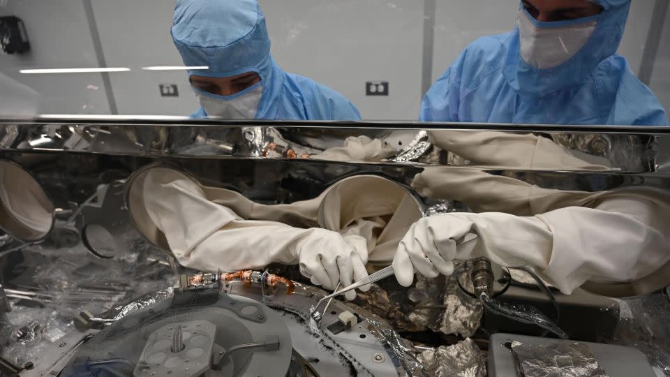 Astromaterials processors Mari Montoya (left) and Curtis Calva use tools to collect asteroid particles from the base of the OSIRIS-REx science canister. - NASA