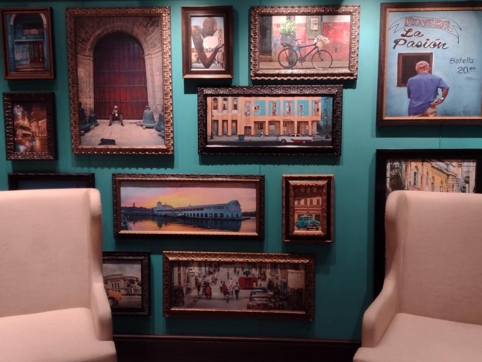 A turquoise wall filled with framed pictures and two armchairs.