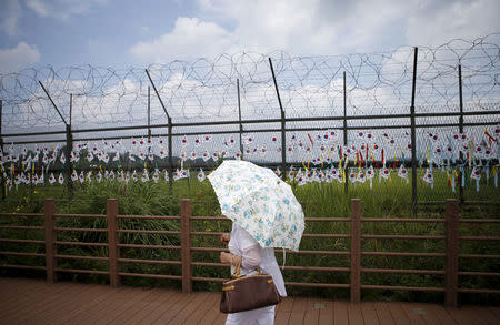 FILE PHOTO: A tourist holding a parasol walks by a barbed-wire fence decorated by South Korean national flags at the Imjingak pavilion near the demilitarized zone separating the two Koreas in Paju, South Korea, August 22, 2015. REUTERS/Kim Hong-Ji/File Photo