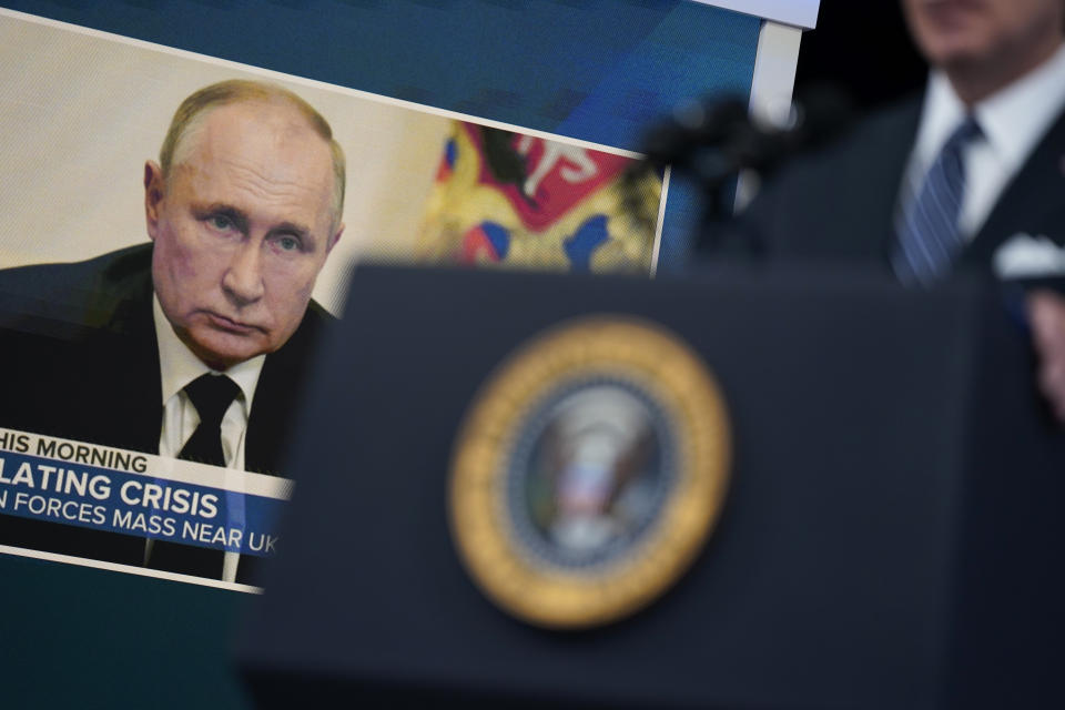 An image of Vladimir Putin appears on a screen behind the U.S. presidential podium, with a headline on TV reading Escalating Crisis.