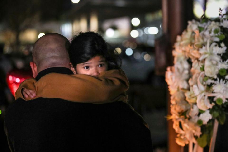 A child is carried as mourners take part in a vigil for victims of a mass shooting at Star Ballroom Dance Studio.