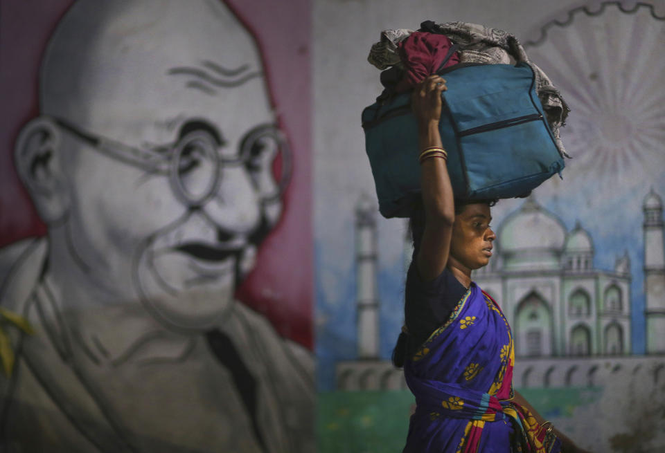 A migrant woman carries her belongings on her head as she walks past a wall painting of Mahatma Gandhi to board a train to her home state, at Hyderabad Railway Station in Hyderabad, India, Saturday, May 23, 2020. India's lockdown was imposed on March 25 and has been extended several times. On May 4, India eased lockdown rules and allowed migrant workers to travel back to their homes, a decision that has resulted in millions of people being on the move for the last two weeks. (AP Photo/Mahesh Kumar A.)