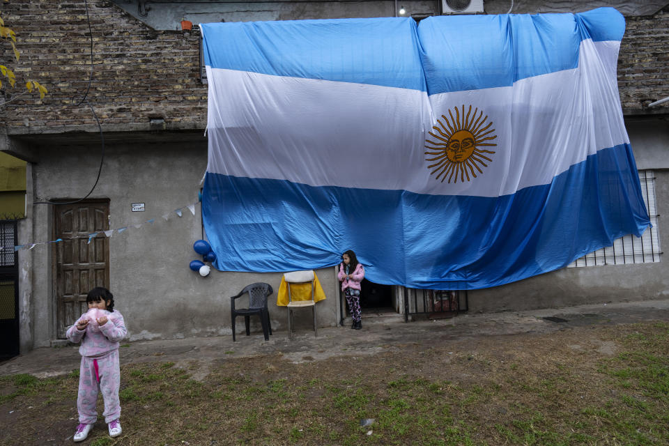 A national flag hangs from the roof of the Shinai soup kitchen run by the Movimiento Evita social organization as a child eats cotton candy, during Independence Day celebrations, in Buenos Aires, Argentina, Wednesday, May 25, 2022. “Three of every 10 homes in the country are beneficiaries of some kind of welfare program,” said Eduardo Donza, researcher at the Social Debt Observatory of the Argentine Catholic University. (AP Photo/Rodrigo Abd)