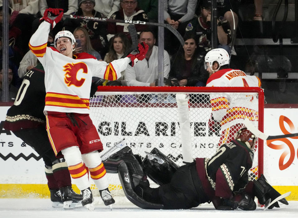 Calgary Flames center Connor Zary, front left, celebrates a goal against Arizona Coyotes goaltender Karel Vejmelka, front right, by Flames defenseman Rasmus Andersson, back right, during the first period of an NHL hockey game Thursday, Jan. 11, 2024, in Tempe, Ariz. (AP Photo/Ross D. Franklin)