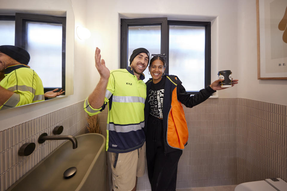 Kyle and Leslie pose smiling with their arms out in their bathroom. 