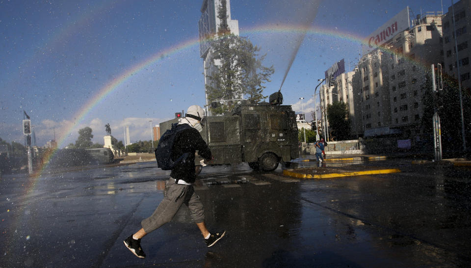 An anti-government protester runs from police water cannons, on the day Chileans vote in a referendum to decide whether the country should replace its 40-year-old constitution, written during the dictatorship of Gen. Augusto Pinochet, in Santiago, Chile, Sunday, Oct. 25, 2020. (AP Photo/Luis Hidalgo)