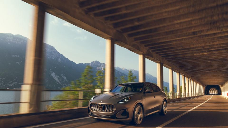 a grey maserati suv drives under a two tier highway bridge alongside a lake