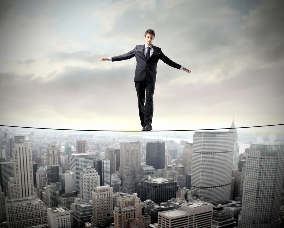 A man in a suit walking a tightrope above a city.