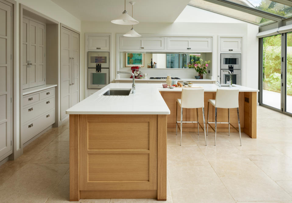 <p> Large spaces don&#x2019;t necessarily equal more walls to design your kitchen around. This spacious kitchen is taken up with one wall of floor-to-ceiling glass windows, leaving L-shaped units on the perimeter. To maximize functionality and storage, the solution was to mirror both runs of units with a large L-shaped kitchen island. </p> <p> &apos;Large areas of glass walling limited the physical area available for kitchen cabinetry,&apos; says Richard Moore, design director of Martin Moore, &apos;so we devised two L-shaped runs, one fitting within the other to create a brilliantly ergonomic solution. The outer runs includes a beautifully fitted out larder cupboard, an appliance cupboard and tall fridge freezer. The return has been cleverly extended visually to run out into the glass roofed area, creating generous space for the large hob, flanked by ovens and extensive storage.&apos; </p> <p> Mirroring the L-shape, the island puts every facility within immediate reach: two warming ovens situated just below worktop height directly face the hob zone for idea functionality. A deep overhang creates an informal seating area. </p>