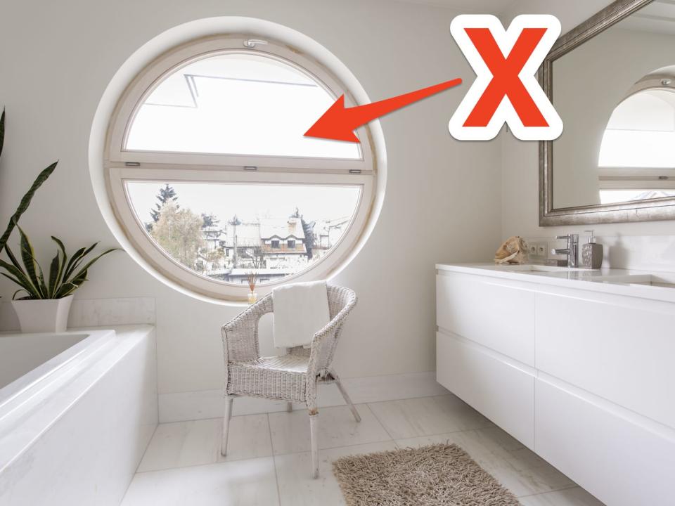 red x and arrow pointing at a round window in a white bathroom