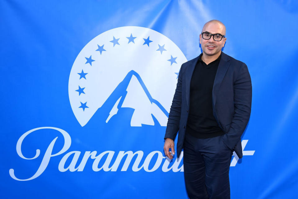 Chris standing in front of a sign with the Paramount logo which is the company's name underneath an illustration of a mountain top within a semicircle of stars