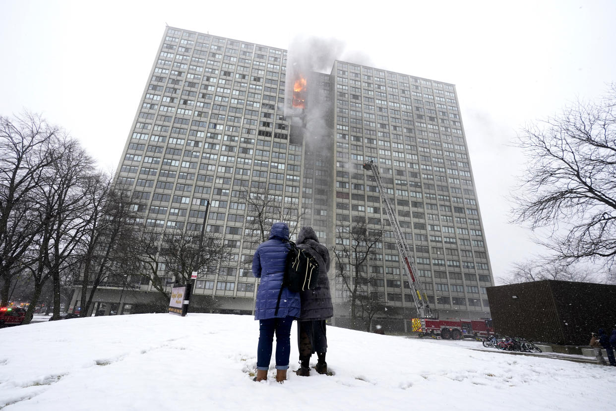 Two women watch as flames leap skyward out of the Harper Square cooperative residential building in the Kenwood neighborhood of Chicago, Wednesday, Jan. 25, 2023. (AP Photo/Charles Rex Arbogast)