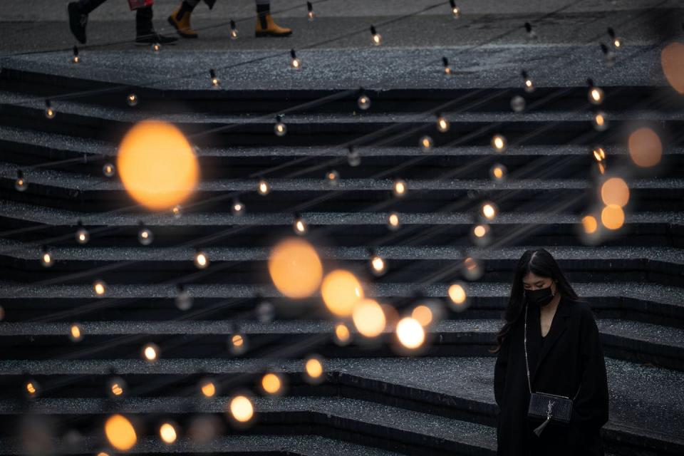 <span class="caption">A woman wearing a face mask to curb the spread of COVID-19 walks through a public plaza as strings of lights are hung overhead in Vancouver in December 2021.</span> <span class="attribution"><span class="source">THE CANADIAN PRESS/Darryl Dyck</span></span>