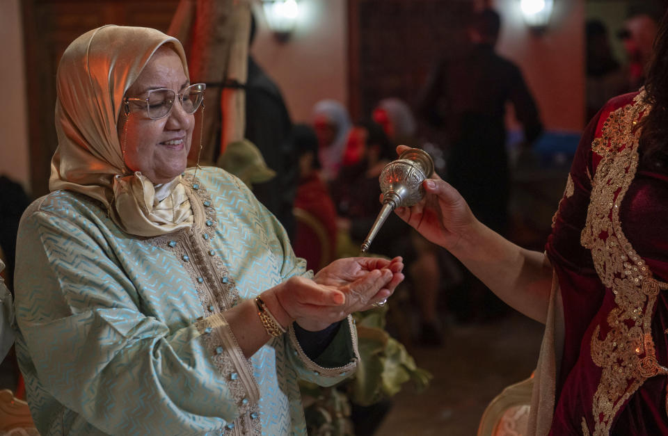 A woman sprinkle orange blossom water after it was distilled, in a cultural center in Marrakech, Morocco, Saturday, March 23, 2024. Moroccan cities are heralding in this year's spring with orange blossoms by distilling them using traditional methods. Orange blossom water is mostly used in Moroccan pastries or mint tea and sprinkled over heads and hands in religious ceremonies. (AP Photo/Mosa'ab Elshamy)