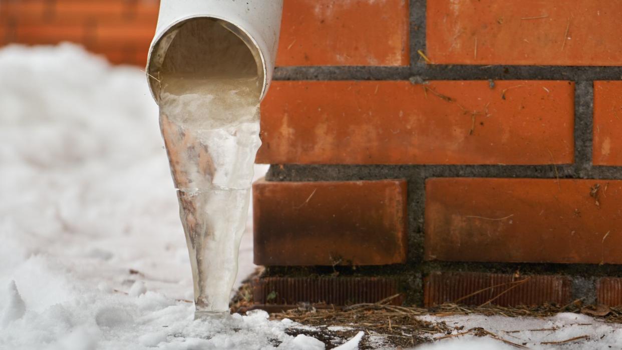 drain pipe with frozen stream of water near brick wall of a cottage outdoors in winter