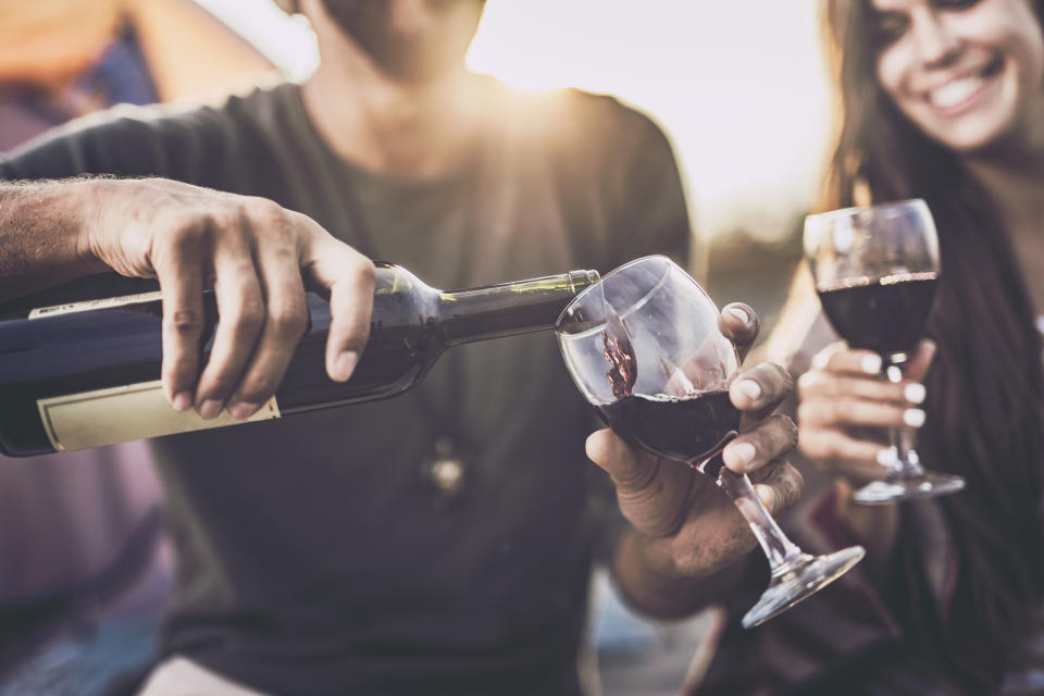 Close up of a couple drinking wine outdoors while man is pouring it into a glass.