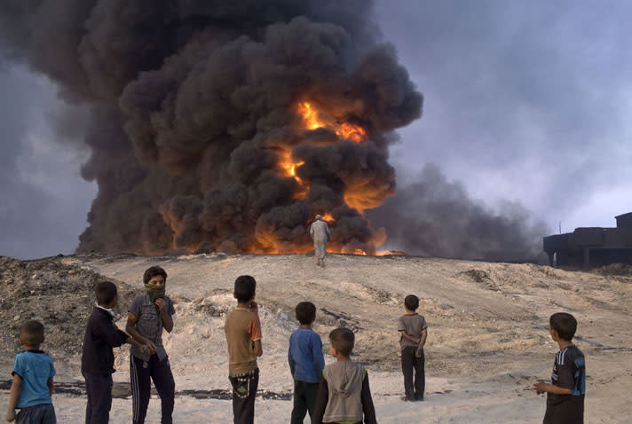 Brennende Ölquelle in Qayyarah In Qayyarah, etwa 50 km südlich von Mossul gelegen, beobachten Schaulustige eine brennende Ölquelle. Zuvor hatten IS-Kämpfer eine Schwefelanlage in Brand gesetzt und so giftige Gase freigesetzt, die sich mit dem Rauch der Ölquelle vermischen. Die Kämpfer wollten mit der brennenden Ölquelle eine Schutzmauer aus Rauch schaffen. (Foto: Marko Drobnjakovic/AP)