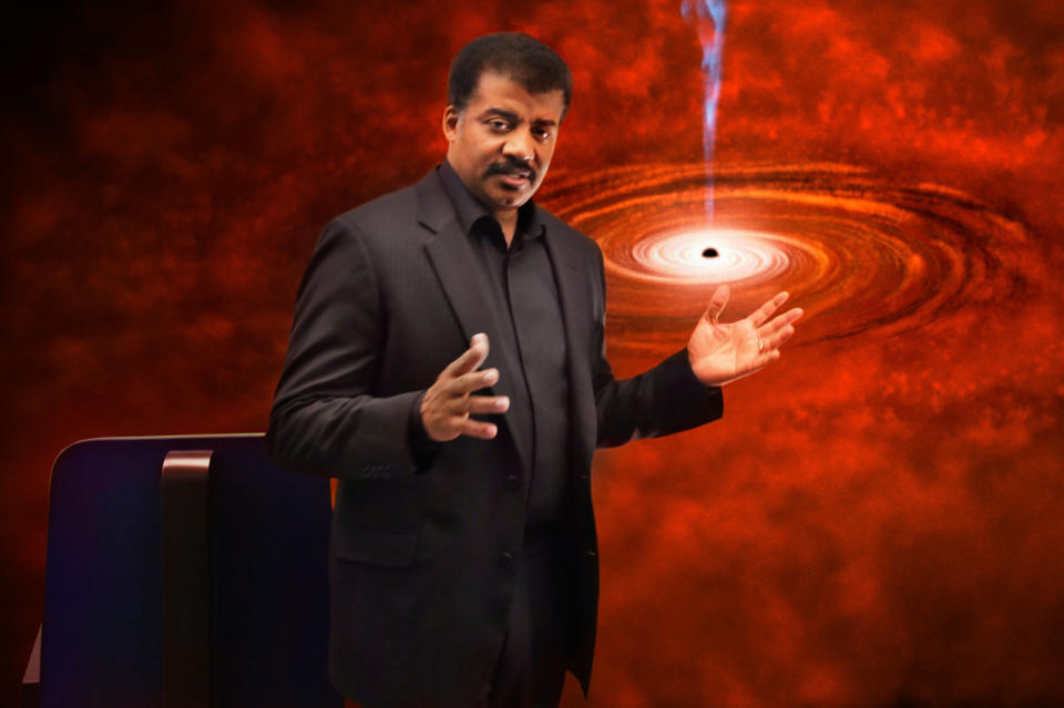 Neil dGrasse Tyson stands before a picture of outer space