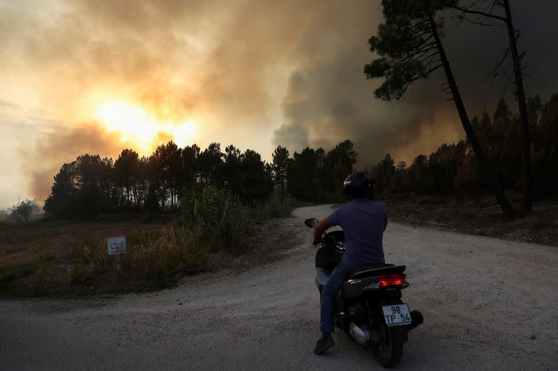 Una persona en motocicleta observa mientras el humo se eleva desde un incendio forestal en Ourem, distrito de Santarém