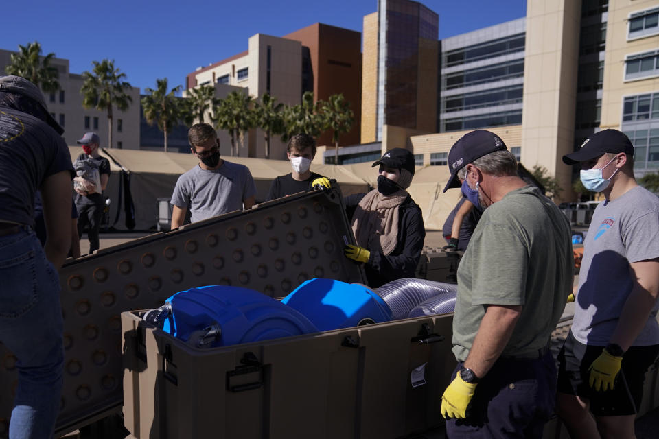 Engineers and volunteers gather around ventilators while setting up a mobile field hospital at UCI Medical Center, Monday, Dec. 21, 2020, in Orange, Calif. California's overwhelmed hospitals are setting up makeshift extra beds for coronavirus patients, and a handful of facilities in hard-hit Los Angeles County are drawing up emergency plans in case they have to limit how many people receive life-saving care. (AP Photo/Jae C. Hong)