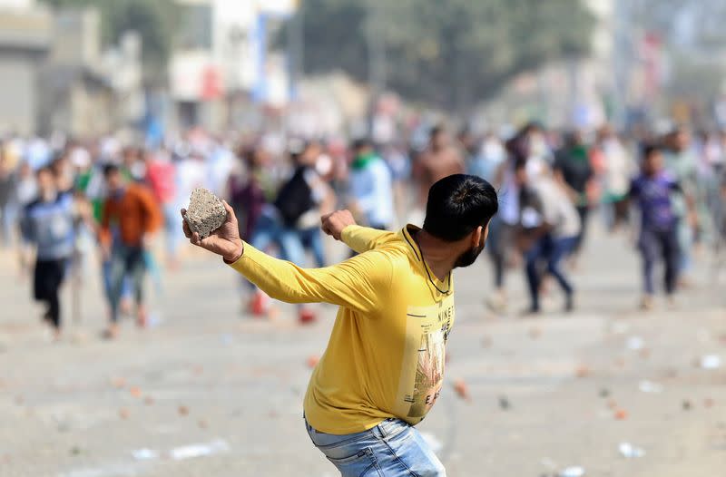 A man supporting a new citizenship law throws a stone at those who are opposing the law, during a clash in New Delhi