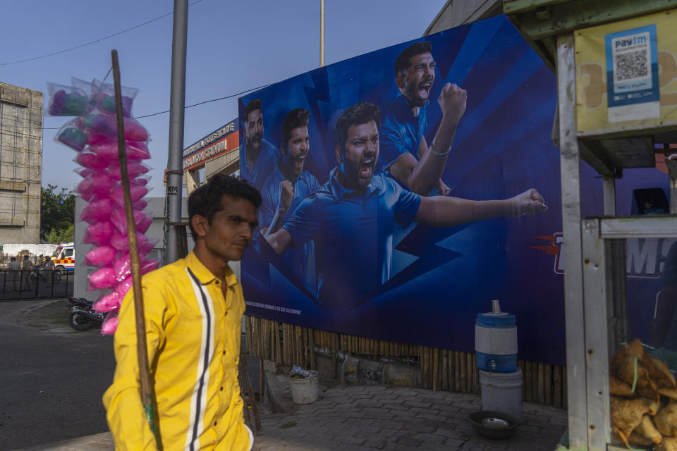 A cotton candy seller walks past a poster of an Indian cricketer outside the Narendra Modi Stadium ahead of the ICC Cricket World Cup in Ahmedabad, India, Tuesday, Oct. 3, 2023. (AP Photo/Rafiq Maqbool)