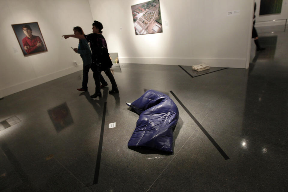 In this Wednesday, Nov. 14, 2012 photo, museum patrons walk past a painted bronze sleeping bag, titled "Nomad," by artist Gavin Turk, at the New Orleans Museum of Art in New Orleans. The piece is part of "Lifelike," a traveling exhibit at the New Orleans Museum of Art through Jan. 27. (AP Photo/Gerald Herbert)