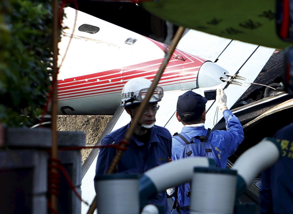 A member of the Japan Transport Safety Board takes pictures of the tail of a small airplane as he inspects the site where the light plane went down in a residential area and burst into flames, in Chofu