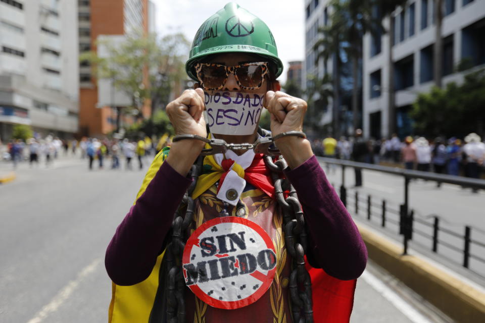 A member of the opposition holds up her handcuffed hands as she joins the start of a rally in Caracas, Venezuela, Tuesday, March 10, 2020. Her signs read in Spanish "No fear," and "Diosdado assassin," referring to ruling party politician Diosdado Cabello. U.S.-backed Venezuelan political leader Juan Guaido will lead a march aimed at retaking the National Assembly legislative building, which opposition lawmakers have been blocked from entering. (AP Photo/Ariana Cubillos)