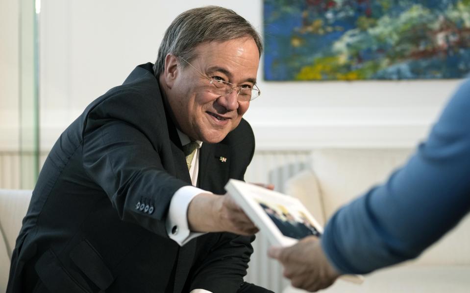 Governor of North Rhine-Westphalia Armin Laschet hands over a book about him during an interview with the Associated Press in his office in Duesseldorf, Germany, Wednesday, June 30, 2021. Laschet, the 60-year-old governor of Germany's most populous state, is the front-runner to succeed Angela Merkel as chancellor in the country's Sept. 26 election. (AP Photo/Martin Meissner)