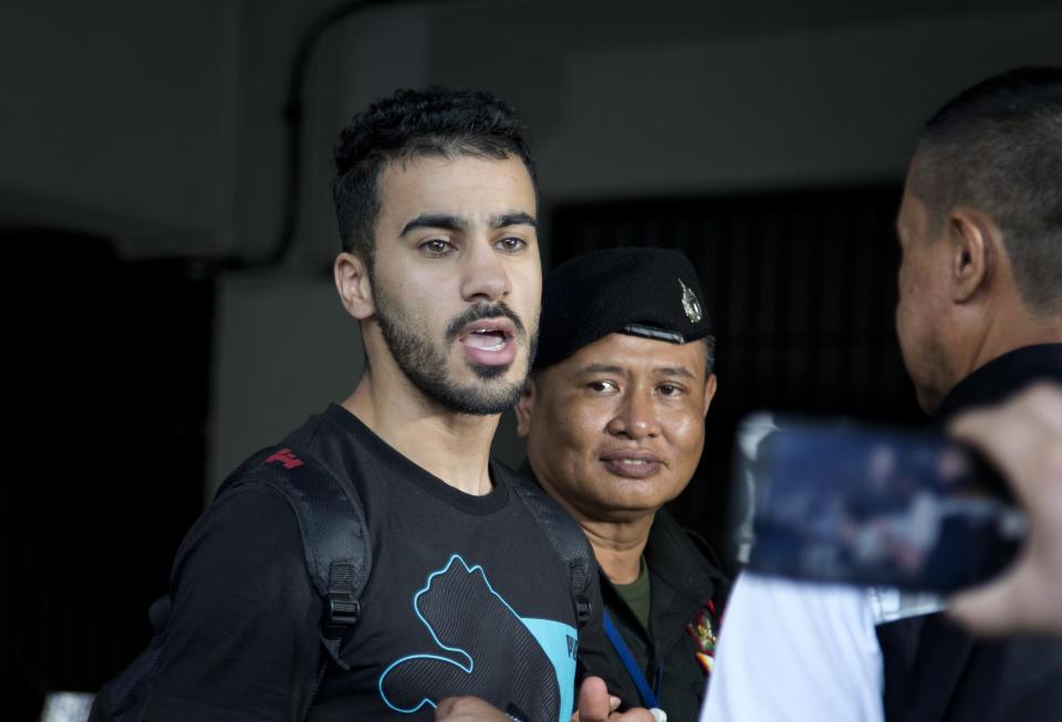Bahraini football player Hakeem al-Araibi, left, answers questions from the waiting journalists as he is brought in to a court in Bangkok, Thailand, Tuesday, Dec. 11, 2018. A Thai court has ruled that the soccer player who holds refugee status in Australia can be held for 60 days pending the completion of an extradition request by Bahrain, the homeland he fled four years ago on account of alleged political persecution. (AP Photo/Gemunu Amarasinghe)