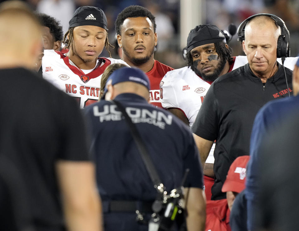 North Carolina State head coach Dave Doeren, right, and players look on as emergency medical personnel aid safety Rakeim Ashford after Ashford was injured during the second half an NCAA college football game against UConn in East Hartford, Conn., Thursday, Aug. 31, 2023. (AP Photo/Bryan Woolston)