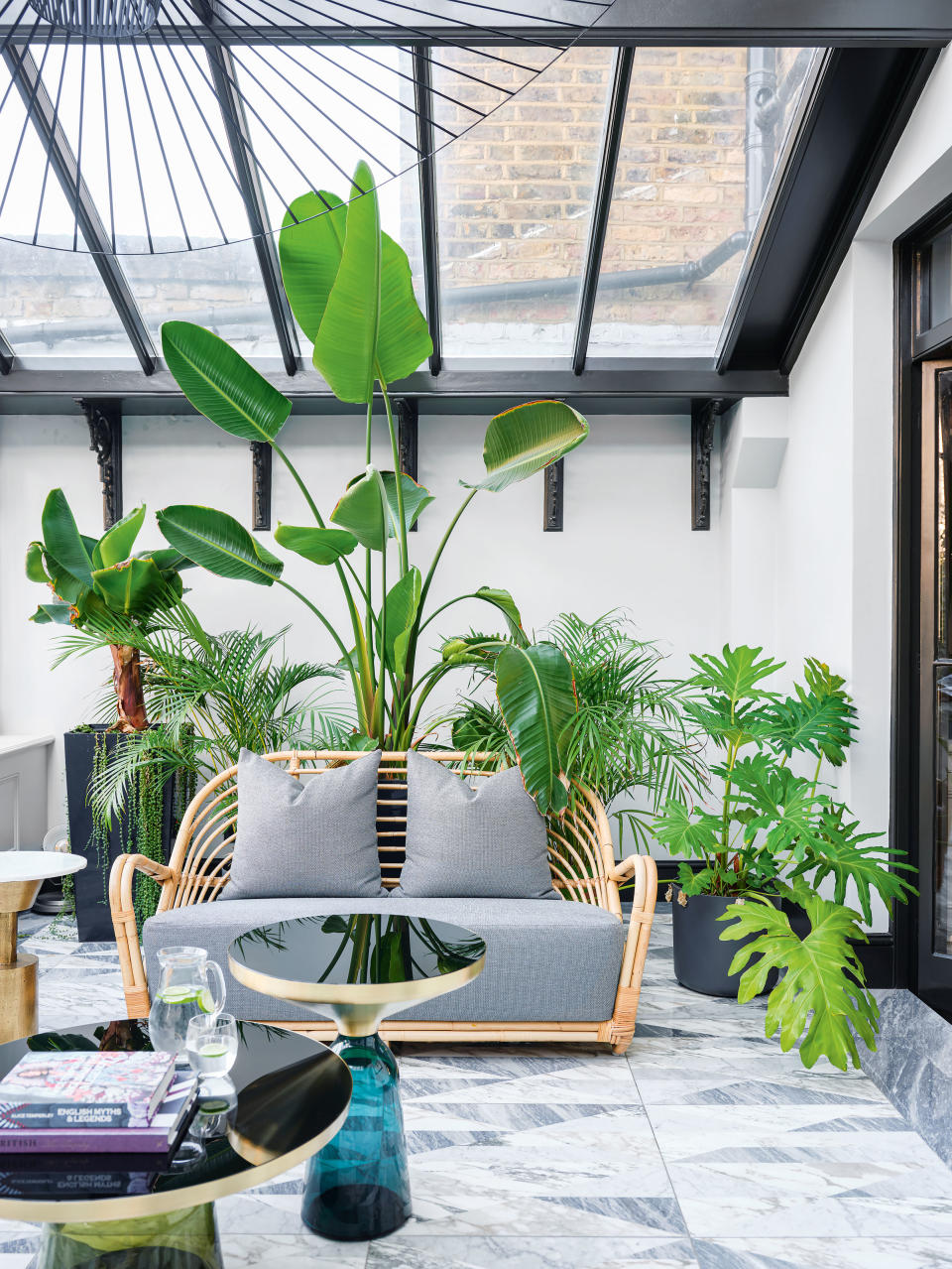 a sunroom filled with plants and rattan furniture