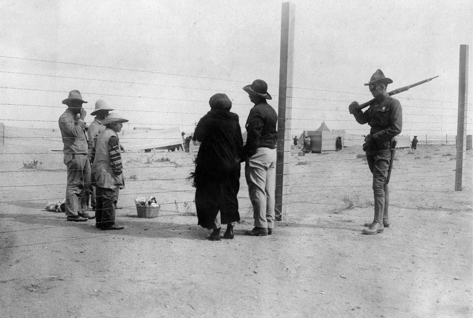 U.S. border guard and Mexicans behind the border fence.