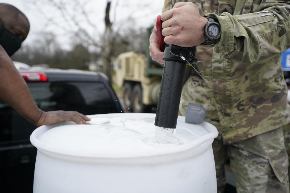 FILE - Mississippi Army National Guard Sgt. Chase Toussaint with the Maneuver Area Training Equipment Site of Camp Shelby, right, fills the 55-gallon water drum with non-potable water for Kenny Taylor, left, March 1, 2021, at a Jackson, Miss., water distribution site. Up to 40,000 Army National Guard soldiers across the country - or about 13% of the force — have not yet gotten the mandated COVID-19 vaccine, and as the deadline for shots looms, at least 14,000 of them have flatly refused and could be forced out of the service. (AP Photo/Rogelio V. Solis, File)