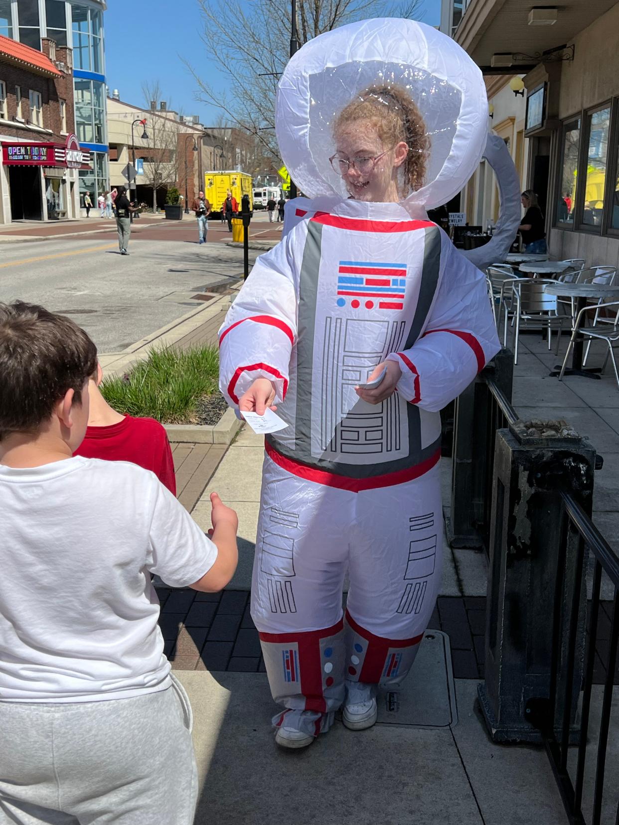 Rachael Vanfossen of Metropolis Popcorn in Cuyahoga Falls passes out coupons for the store Monday during EclipseFest 2024. She is dressed as a solar eclipse astronaut.
