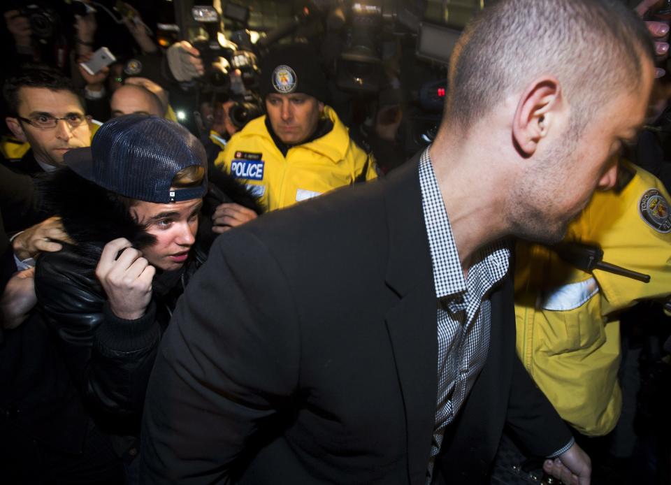 Canadian musician Justin Bieber is swarmed by media and police officers as he turns himself in to city police for an expected assault charge, in Toronto, on Wednesday, Jan. 29, 2014. A police official said the charge has to do with an alleged assault on a limo driver in December. (AP Photo/The Canadian Press, Nathan Denette)